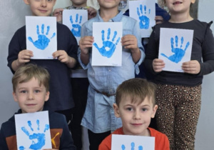 Dzieci z oddziału przedszkolnego prezentują wykonane przez siebie niebieskie odciski dłoni
