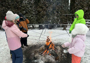 Grupa dzieci przy ognisku piecze kiełbaski