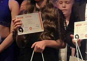 Dziewczynka podczas gali pozuje do zdjęcia z dyplomem i nagrodą