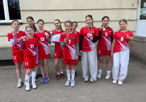 Dziewczyny przed budynkiem szkoły w strojach reprezentacyjnych z dyplomem i medalami