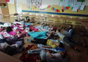 Uczniowie klasy 2b na podłodze wśród koców i poduszek podczas seansu filmowego