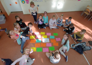 Dzieci siedzą na podłodze w kole, w środku którego ułożone są kolorowe kartki z napisami związanymi z dobrym zachowaniem