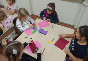 Dzieci siedzą przy stolikach i wycinają kolorowe serduszka