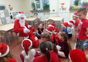 Dzieci ubrane na czerwono siedzą przed Mikołajem
