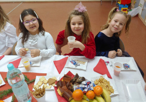 Dziewczynki siedzą przy stole, piją i jedzą