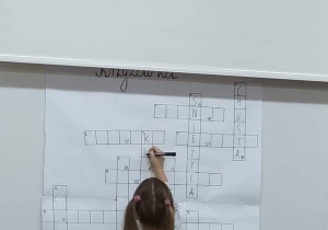 Dziewczynka wpisuje hasło do krzyżówki zawieszonej na tablicy