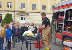 Strażak prezentuje dzieciom zgromadzonym przy wozie sprzęt stażacki