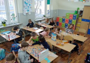 Uczniowie siedzą przy stolikach i układają puzzle