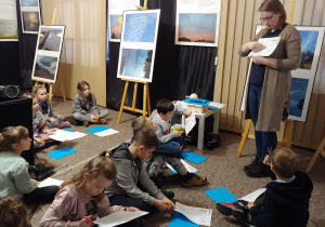 Pracownica muzeum przekazuje dzieciom instrukcję wykonania książeczki o chmurach.