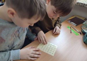 Chłopcy dotykają palcami kartkę z alfabetem Braille'a