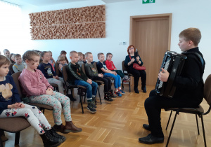 Uczniowie zgromadzeni w sali słuchają prezentacji akordeonowej
