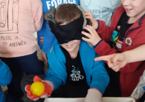 Chłopiec z zakrytymi oczami i rękawicami znalazł wśród klocków plastikową piłeczkę