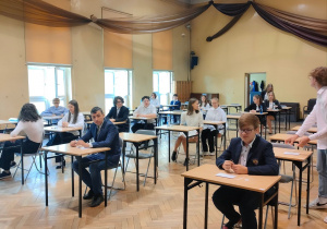 Uczniowie siedzą przy stolikach na sali gimnastycznej przed rozpoczęciem egzaminu pisemnego