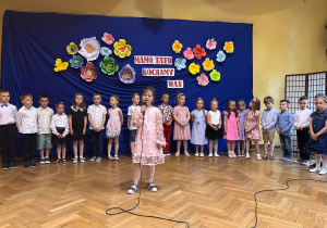 Lila Bernacka stoi przed grupą dzieci i wykonuje piosenkę dedykowaną rodzicomLila Bernacka stoi przed grupą dzieci i wykonuje piosenkę dedykowaną rodzicom