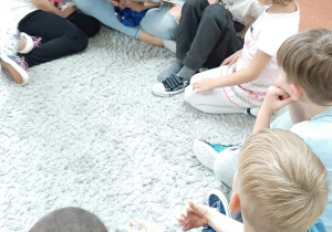 Dzieci siedzą na dywanie i słuchają