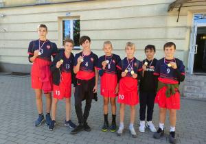 Chłopcy pozują do zdjęcia przed budynkiem szkoły z medalami