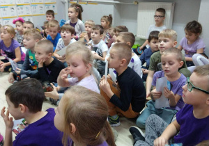 Dzieci siedzą na podłodze i słuchają prelekcji