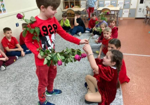 Uczeń z oddziału przedszkolnego rozdaje czerwone róże