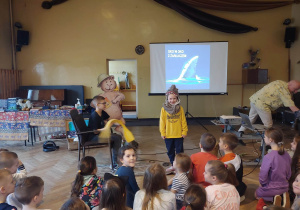 Uczeń w roli kajakarza i uczennica przebrana za rekina odgrywają role przed uczniami z innych klas.