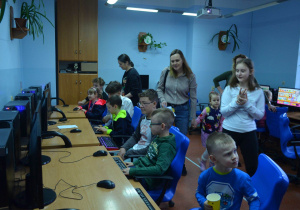 Dzieci siedzą przed monitorami komputerów w sali informatycznej