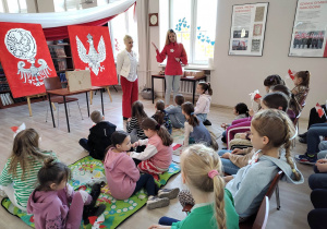 Dziewczynki siedzą na podłodze i słuchają historii polskich symboli narodowych.