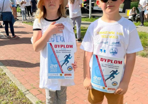 Dwoje dzieci w koszulkach promujących bieg z dyplomami