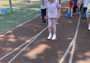 Dziewczynka przenosi piłeczkę między kolanami na boisku szkolnym