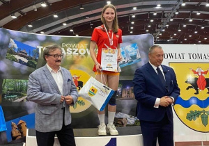 Tosia Krawczyk stoi na pierwszym stopni podium z medalem dyplomem i nagrodami