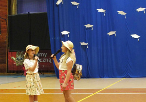 Dwie dziewczynki w letnich przebraniach w kapeluszach śpiewają piosenkę wakacyjna