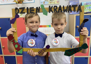 Dwóch chłopców pozuje do zdjęcia w foto-ramce z napisem DZIEŃ KRAWATA
