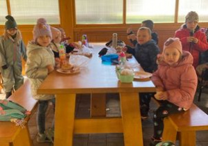 Dzieci siedzą przy dużym stole i jedzą kiełbaski