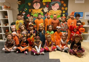 Dzieci z grupy 0a w strojach jesiennych na tle dekoracji jesiennej