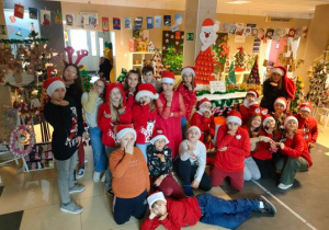 Klasa 5b ubrana na czerwono na zdjęciu grupowym w holu szkoły przy świątecznej dekoracji
