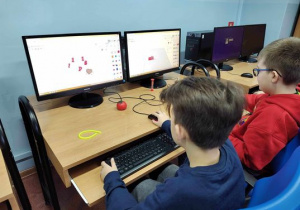 Dwóch chłopców siedzi przed monitorami, na których widać tworzenie własnych modeli 3D