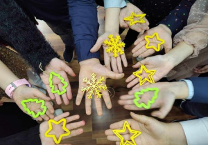 Świąteczne zawieszki 3D przezntowane na dłoniach i uczniów (zielone choinki, żółte śnieżynki i gwiazdki)