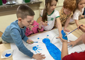 Dzieci zebrane wokół stołu odciskają dłonie pomalowane na niebiesko