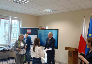 Dziewczynka odbiera list gratulacyjny i nagrodę z rąk Łódzkiego Kuratora Oświaty